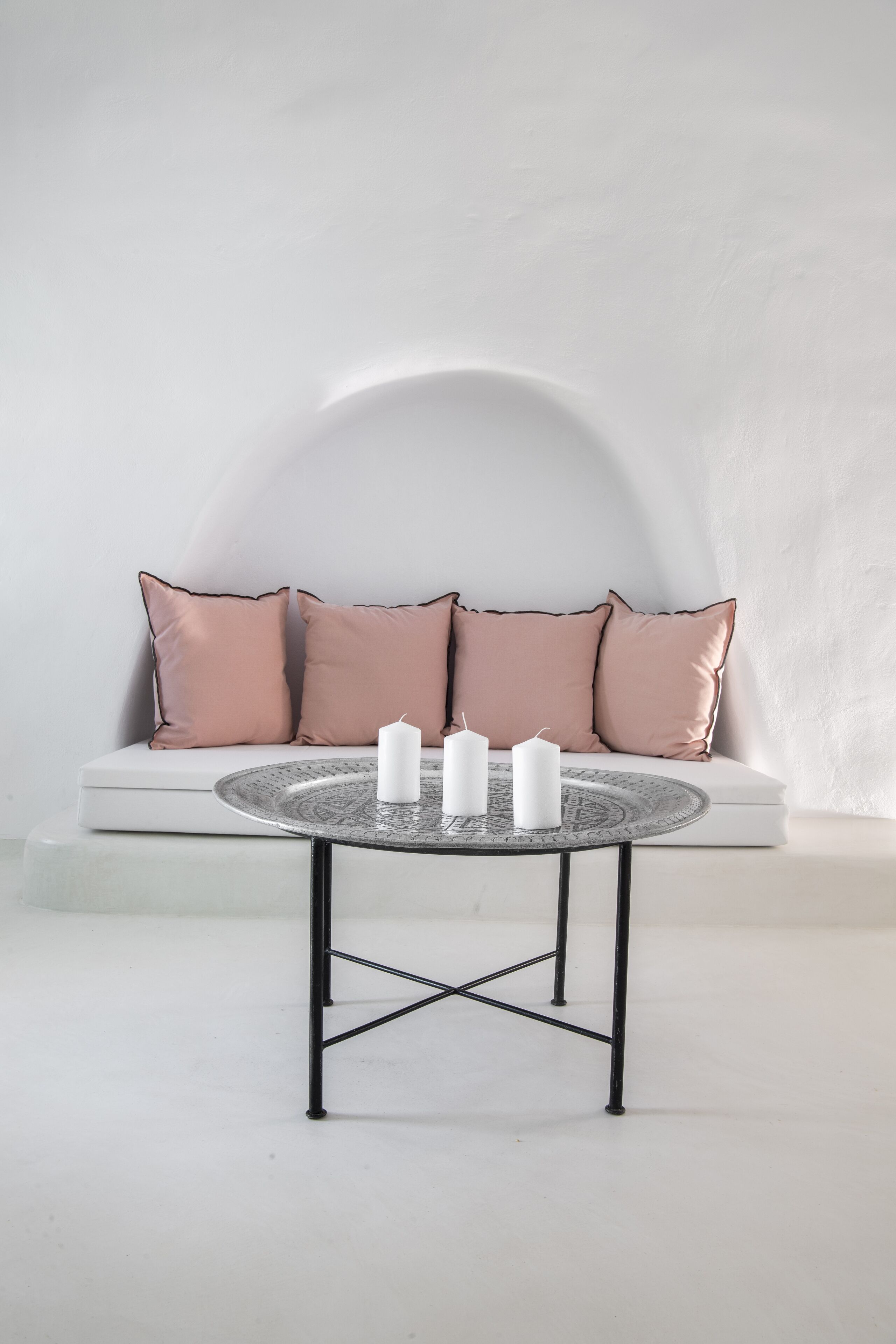 A minimalist room with a round table, three white candles, and a white sofa with pink cushions.