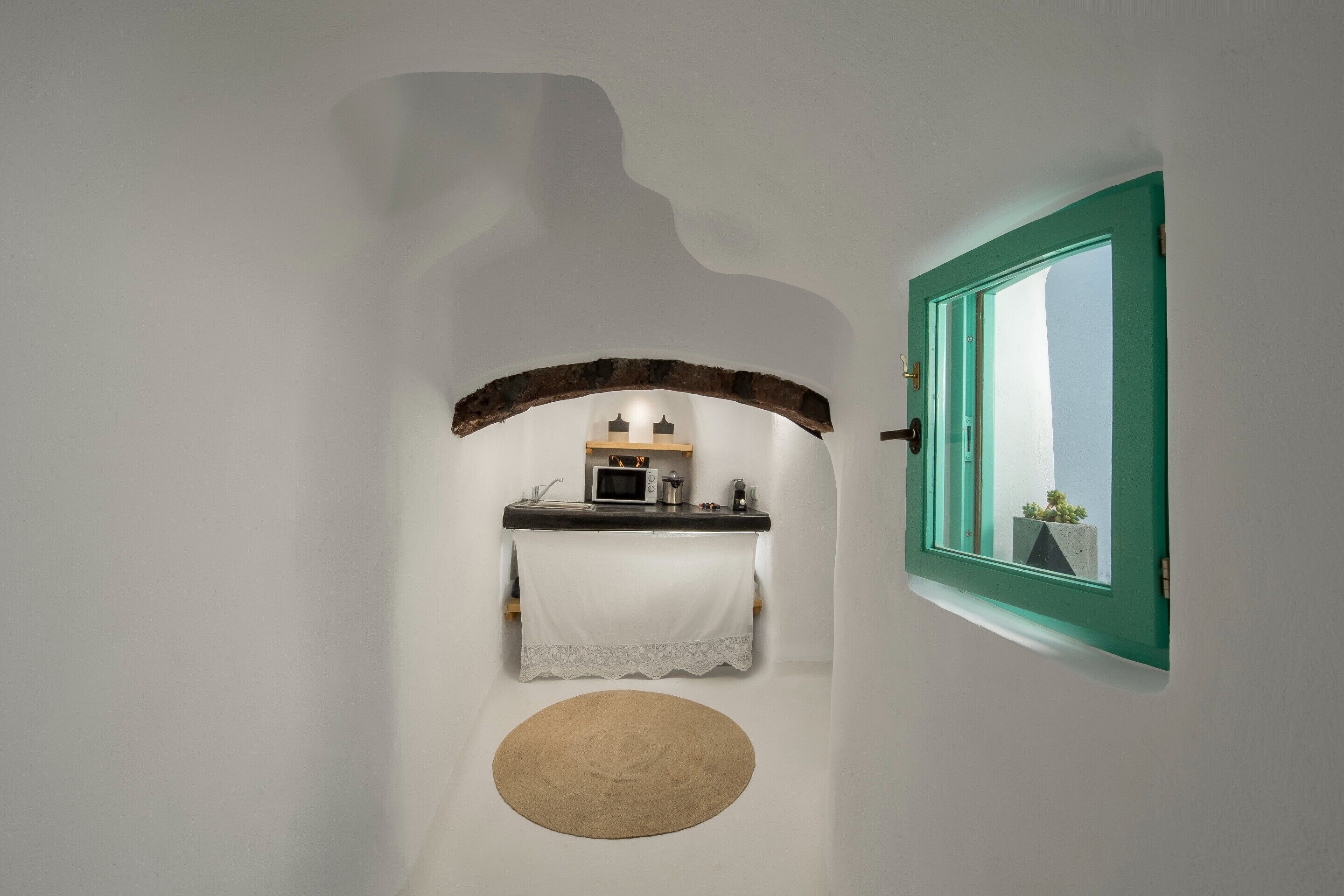 Un pasillo estrecho con una zona de cocina, un tapete redondo y una ventana de marco color turquesa.