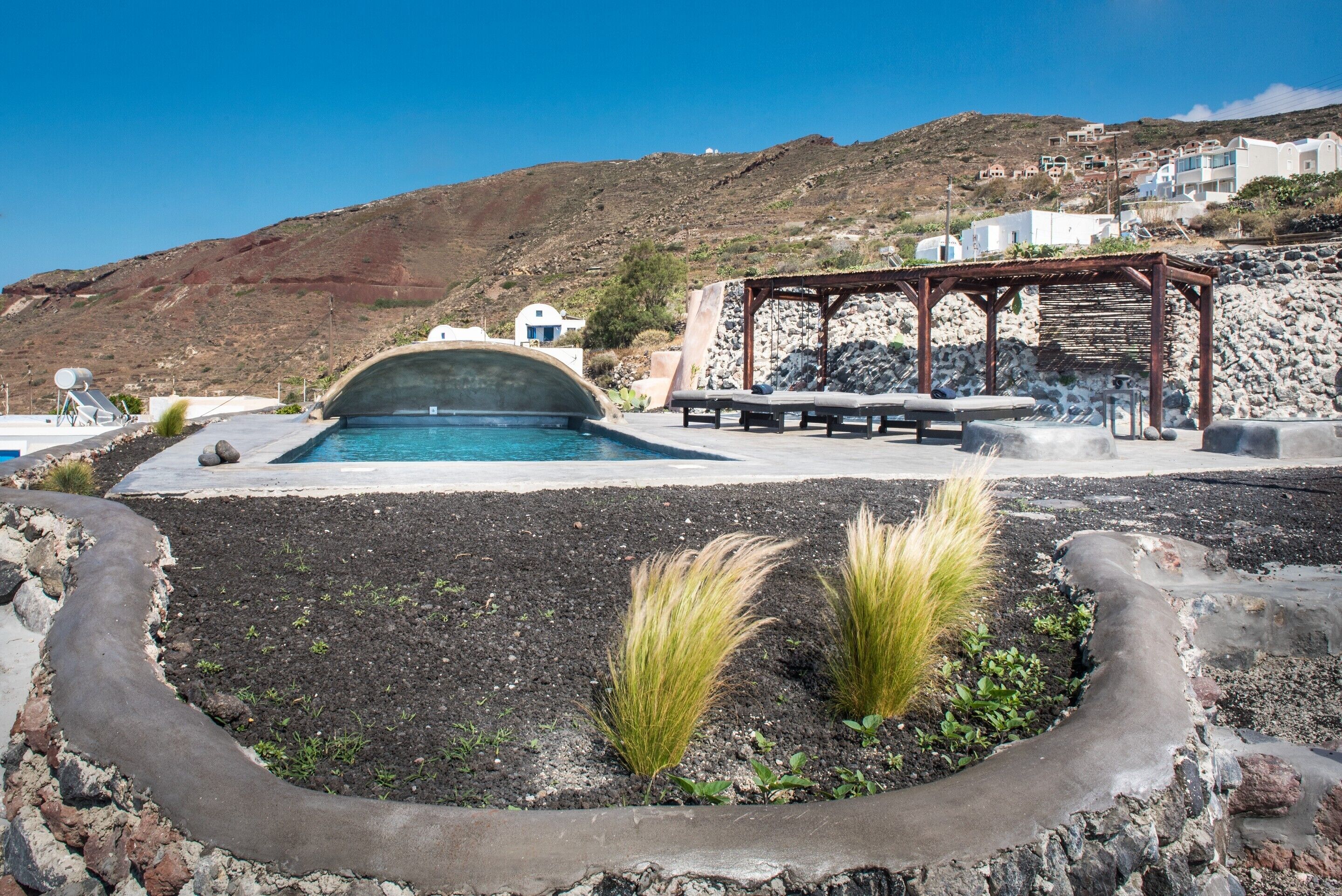 A pool area with a stone structure, lounge chairs, and a view of a hillside with buildings.