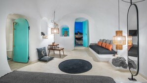 A modern living room with a sofa, a round rug, and a dining area with a table and chairs. - Sophia Finikia Villas (Santorini)