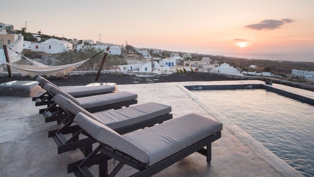 A rooftop pool area with lounge chairs and a view of white buildings in the background. - Sophia Finikia Villas (Santorini)