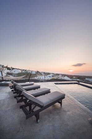 A rooftop pool area with lounge chairs and a view of white buildings in the background. - Sophia Finikia Villas (Santorini)