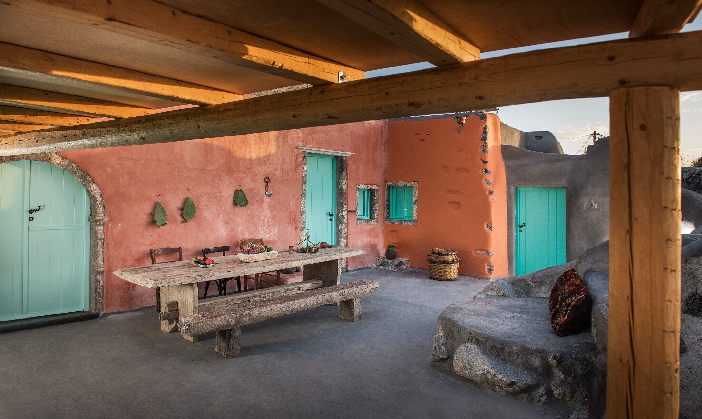 Une terrasse extérieure avec une table et des bancs en bois rustique, entourée de murs et de portes en pierre.