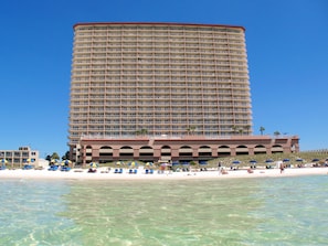 Un grand hôtel à plusieurs étages, doté de balcons, situé près d’une plage à l’eau claire et équipée de transats.