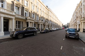 A street lined with historic buildings, parked cars, and a clear sky.