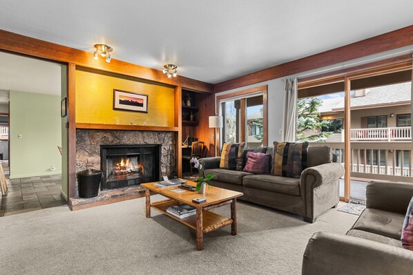 A living room with a fireplace, a sofa, a coffee table, and a view of the outside.
