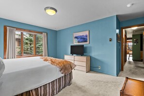 A bedroom with a bed, a dresser, a television, and a window with curtains.