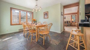 A dining area with a round table and wooden chairs, a chandelier, and large windows. - RMR: Teewinot A2 Condo in Teton Village (Teton Village)