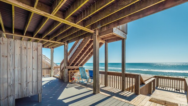 Une terrasse en bois avec un escalier menant à un balcon d’où l’on a vue sur l’océan.