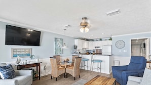 A modern living room with a TV, dining area, and kitchen. - 21- Best Views of the BEACH from the balcony of this beautiful condo! (Destin)