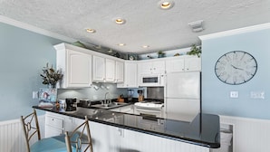 A kitchen with white cabinets, a black countertop, and a clock on the wall. - 21- Best Views of the BEACH from the balcony of this beautiful condo! (Destin)