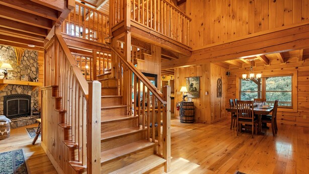 A wooden interior with a staircase, a fireplace, a dining area, and a large window. - Large Cabin Near Downtown Blowing Rock (Blowing Rock)