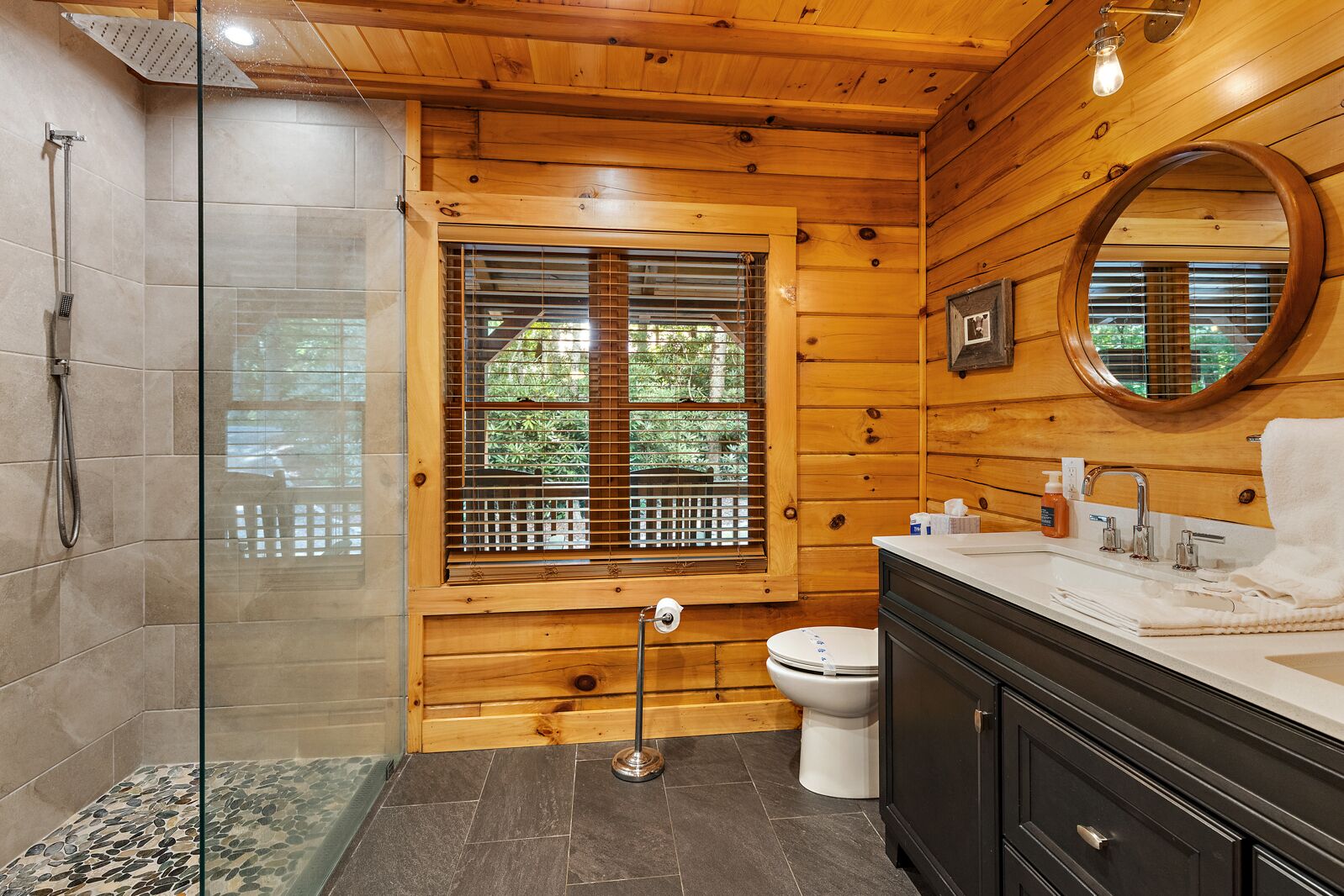 A wooden cabin bathroom with a glass shower enclosure, a toilet, and a vanity with a mirror.