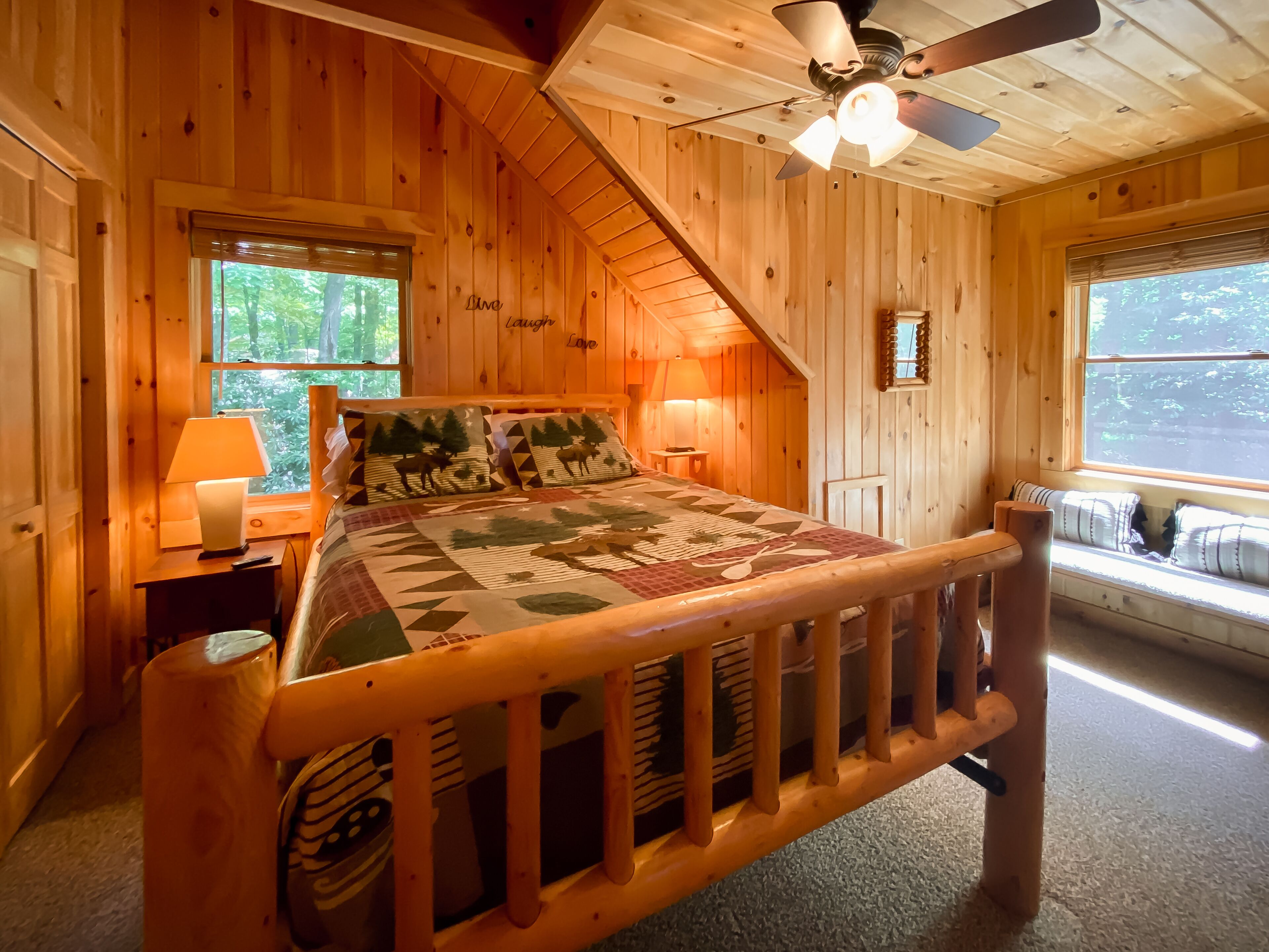 Ein Schlafzimmer einer Holzhütte mit Bett, Fenster, Deckenventilator und Nachttisch.