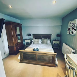 A bedroom with a large bed, wooden headboard, two bedside tables, a radiator, and a cabinet. - The Fleur de Lys Inn (Wimborne)