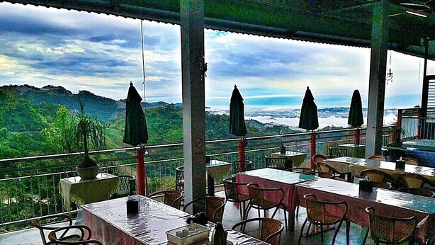 Un espacio para comer al aire libre con mesas, sillas, sombrillas y vistas a las montañas.