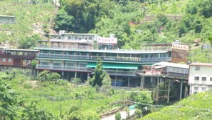 Un edificio de varios pisos con balcones, rodeado de vegetación exuberante y colinas.
