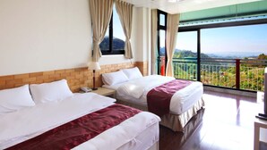 Habitación de hotel con dos camas, cabecera de ladrillo, mesita de noche, lámpara y un ventanal con vistas al paisaje.