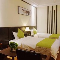 Habitación de hotel con dos camas, una mesita de noche, una lámpara, un cuadro en la pared y una planta en maceta.