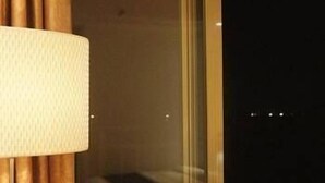 A hotel room with a large window, a bed, and a lamp. - Mingju Holiday Hotel (Yangjiang)
