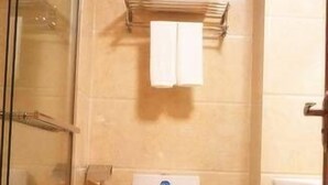 A bathroom with a toilet, a glass shower enclosure, and a towel rack with two towels. - Mingju Holiday Hotel (Yangjiang)