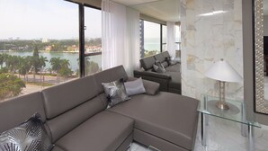 Una sala de estar moderna con un sofá seccional, una mesa de centro de vidrio y vistas a un cuerpo de agua y un paisaje urbano.