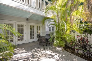 A covered patio with a table and chairs, surrounded by lush greenery and a white picket fence. - CAPTAIN'S WHEEL at The Truman Annex in Key West (Key West)