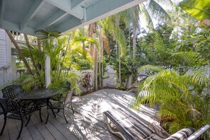 A covered patio with a wooden deck, metal chairs, and a striped bench. - CAPTAIN'S WHEEL at The Truman Annex in Key West (Key West)