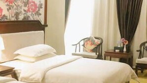 A hotel room with two beds, a floral wall decoration, a chair, a small table, and a window with curtains.
