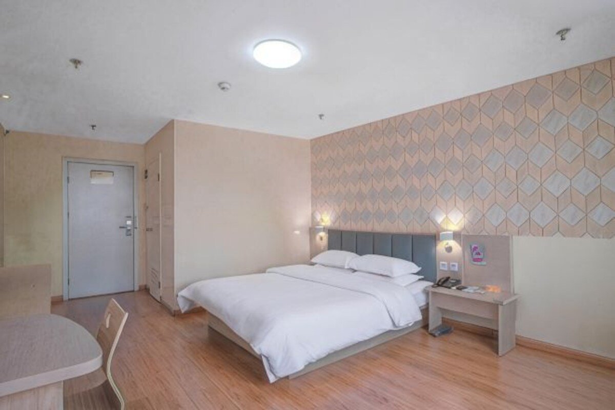Habitació d'hotel amb llit, taulella, escriptori, cadira i paper de paret estampat.