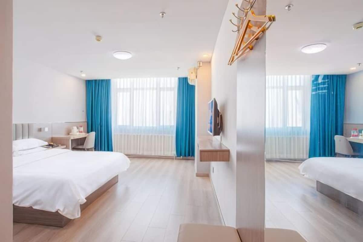 Una habitación de hotel moderna con dos camas, un escritorio, una silla, un televisor y un amplio ventanal con cortinas.