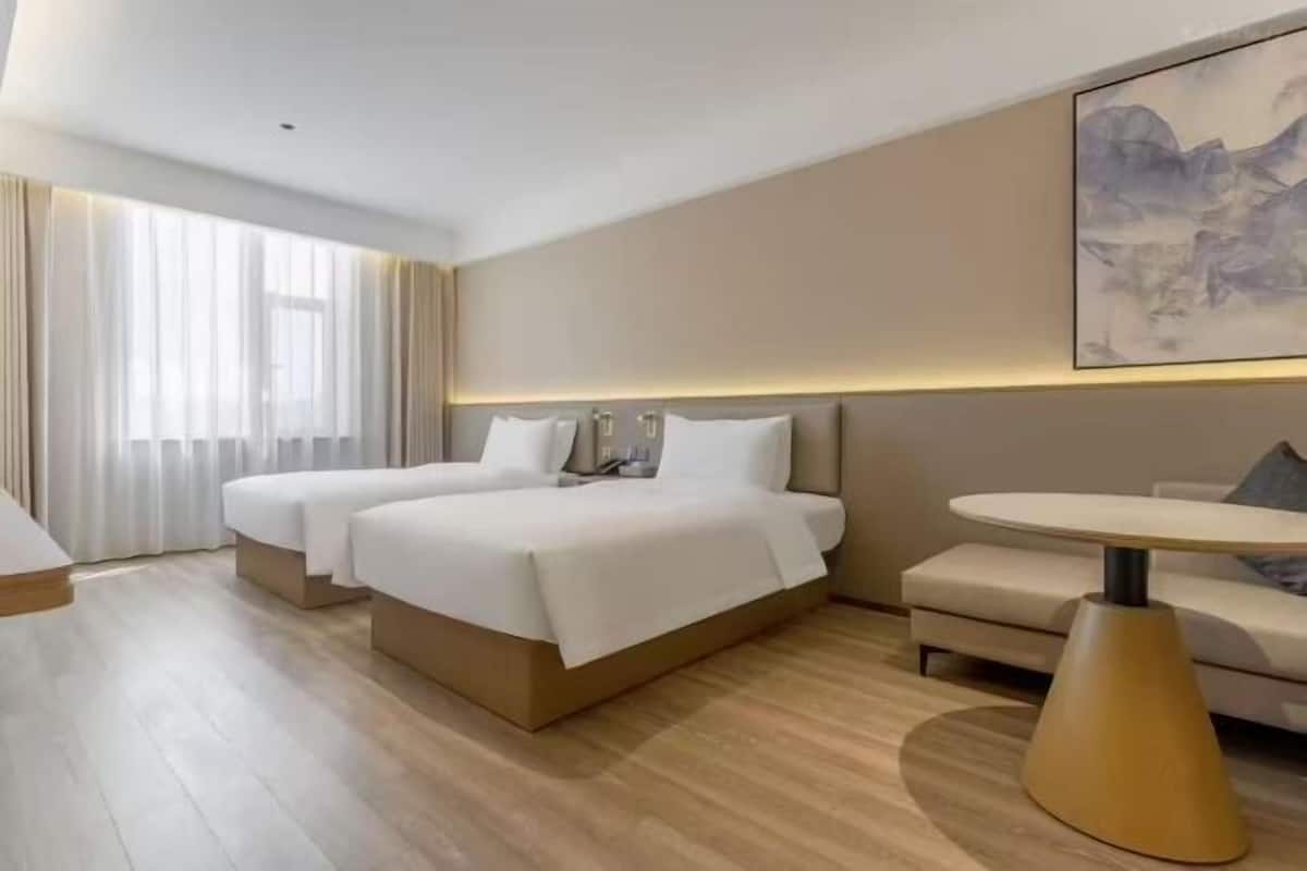 Habitación de hotel con dos camas, un pequeño sofá, una mesa redonda y un cuadro en la pared.