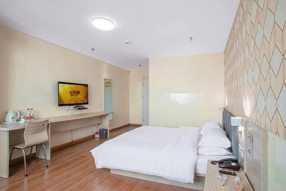 Habitación de hotel con cama, escritorio, silla, televisión y pared con baldosas.