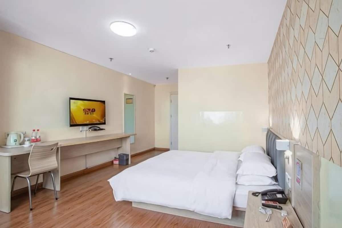 A hotel room with a bed, desk, chair, television, and a tiled wall.