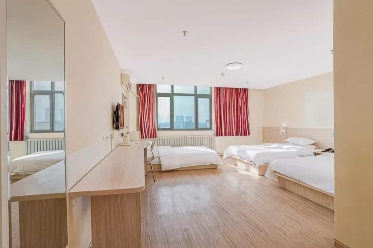 Habitación de hotel con un espejo grande, dos camas, un escritorio y vistas de la ciudad a través de amplios ventanales.