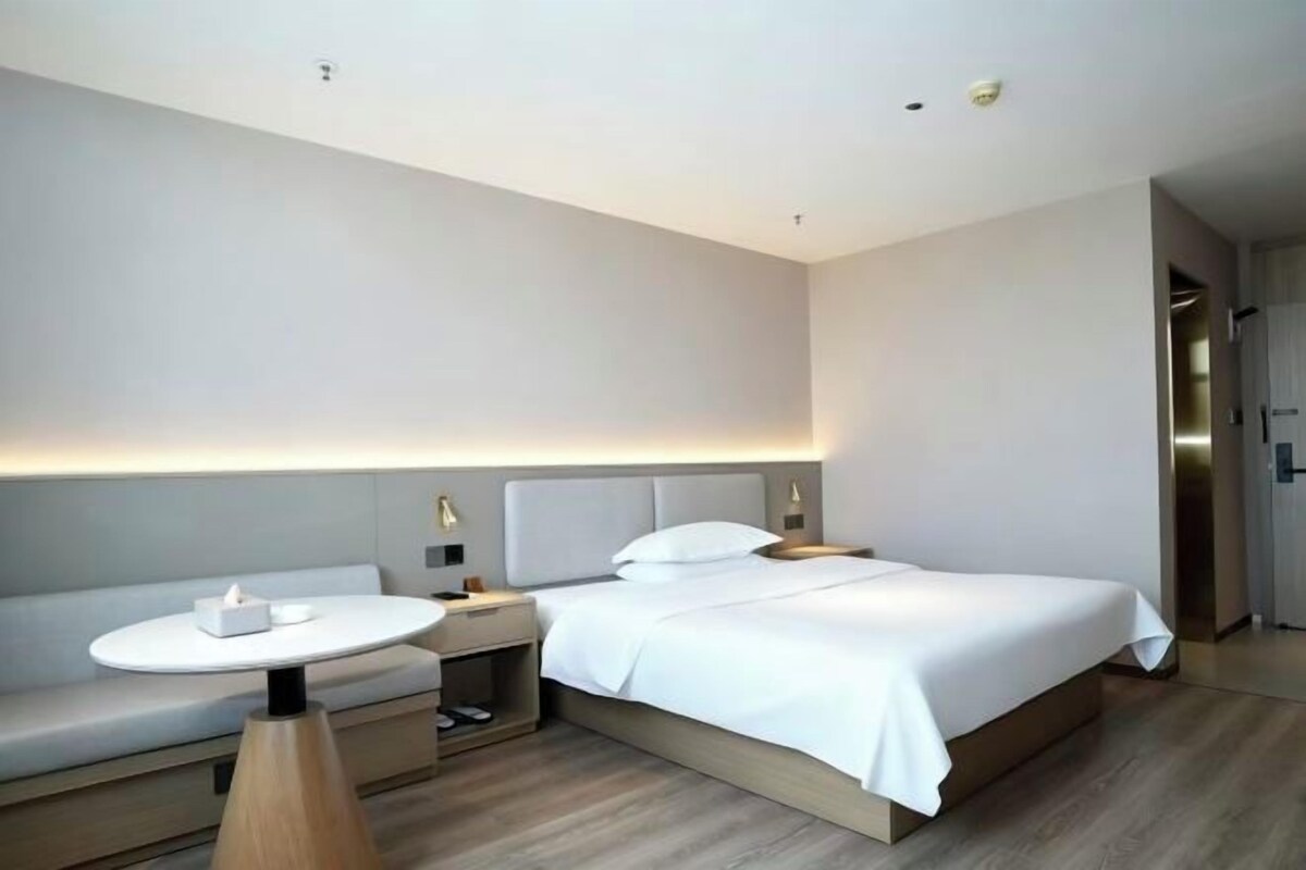 Una habitación de hotel moderna con cama, mesita de noche y una pequeña mesa redonda con lámpara.