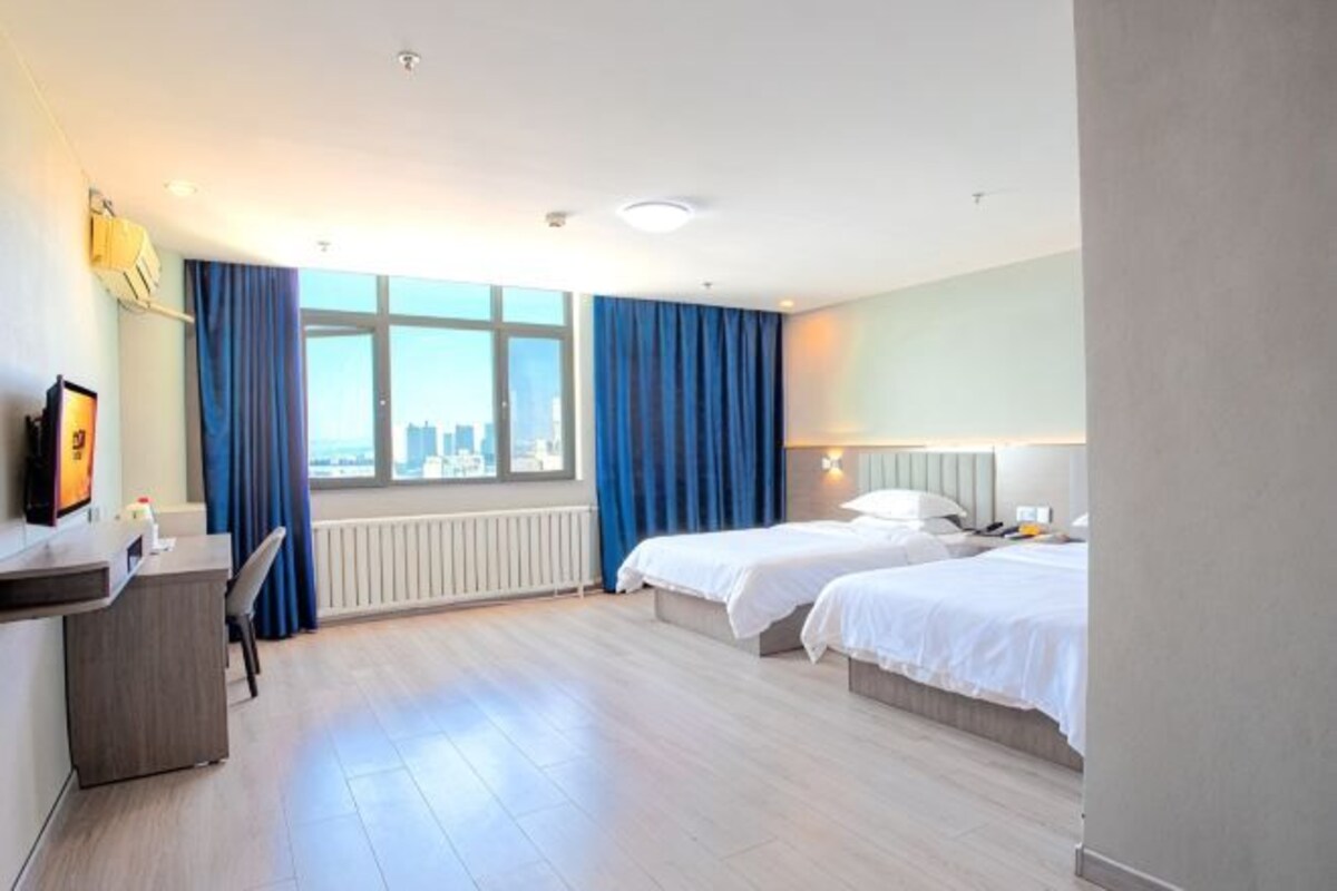 Habitació d'hotel amb dos llits, una taula de nit, una cadira, una finestra amb cortines i vista a la ciutat.