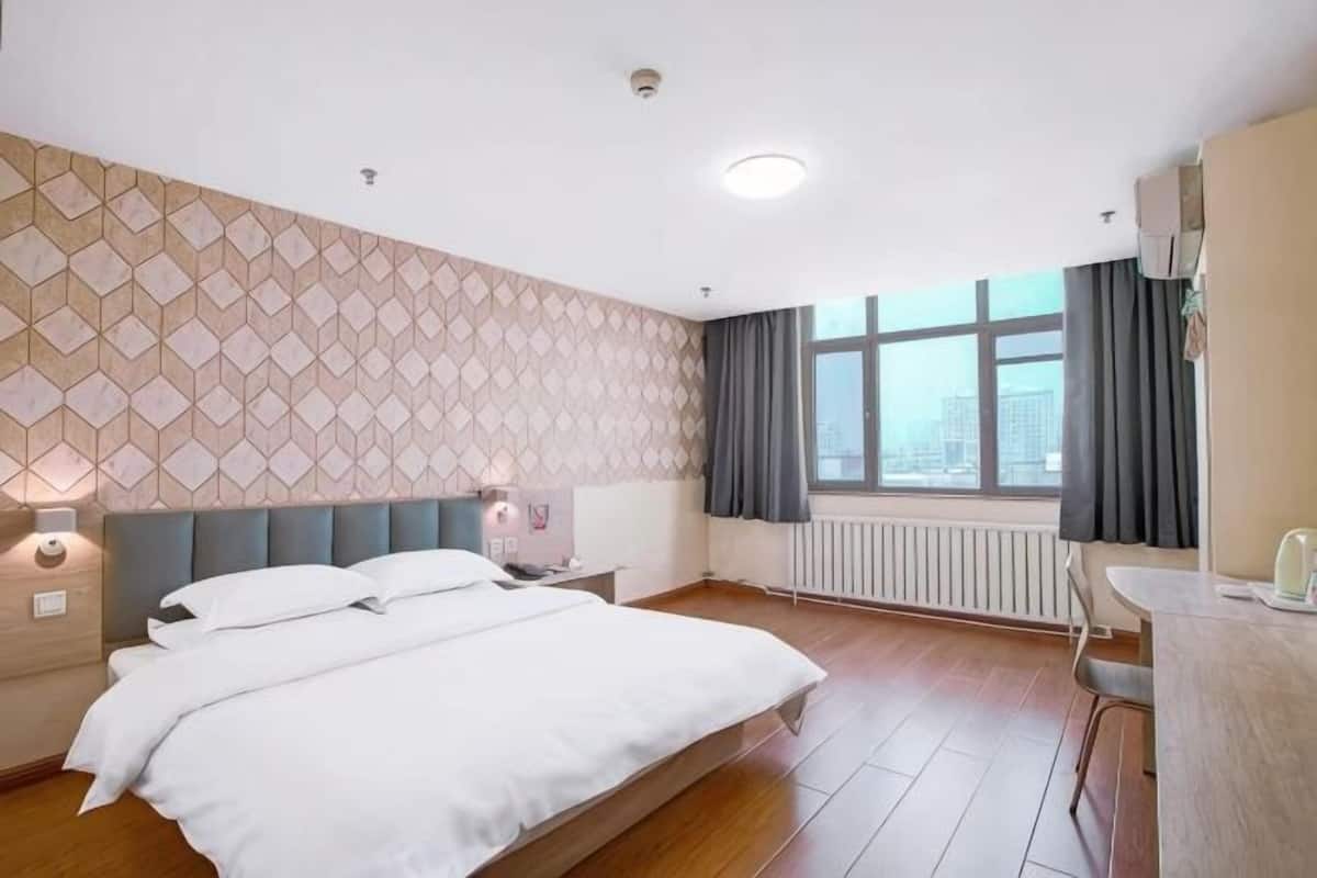 Habitación de hotel con cama, escritorio, ventana con cortinas, radiador y pared estampada.