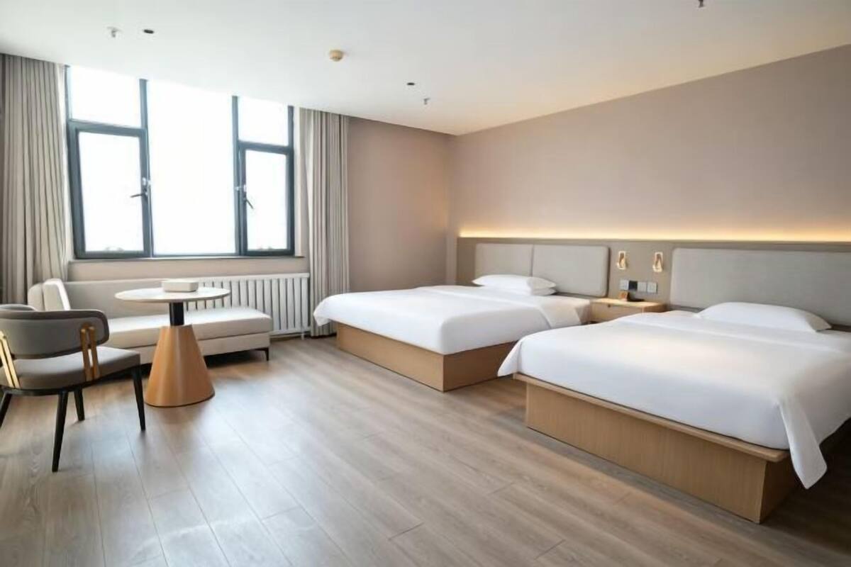 Habitación de hotel con dos camas, un sofá, una mesa y un ventanal grande.