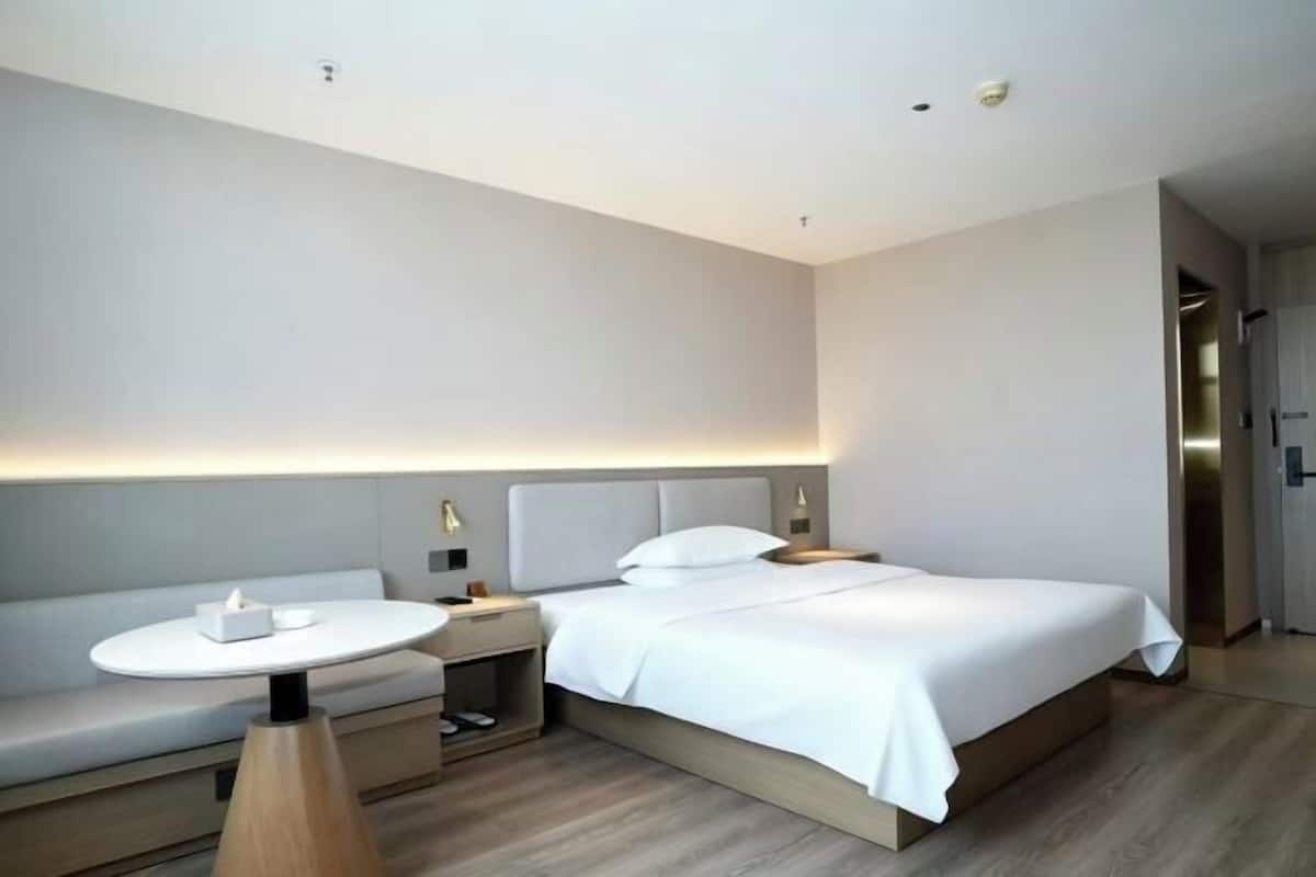 Una habitación de hotel moderna con cama, mesita de noche y una pequeña mesa redonda con lámpara.