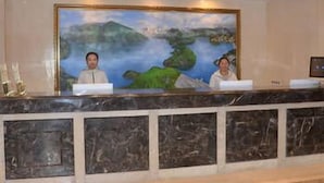 A reception desk with two staff members, a large landscape painting, and a marble counter. - Jinjiang Jinqiao Hotel (Liangshan Yi)