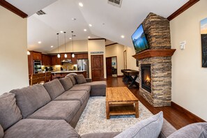 A living room with a stone fireplace, a large sectional sofa, and a wooden coffee table.