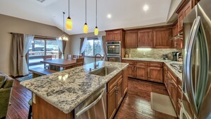 Una cocina moderna con encimeras de granito, electrodomésticos de acero inoxidable, armarios de madera e iluminación colgante.