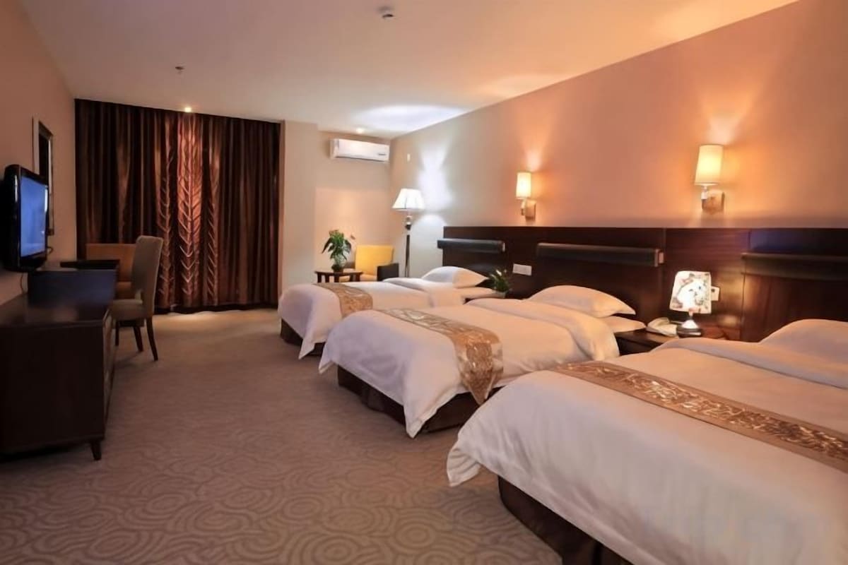 A hotel room with three beds, a desk, a television, and a lamp.