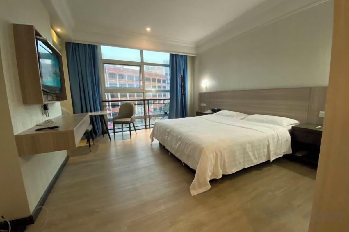 A hotel room with a bed, desk, chair, TV, and a window with curtains.