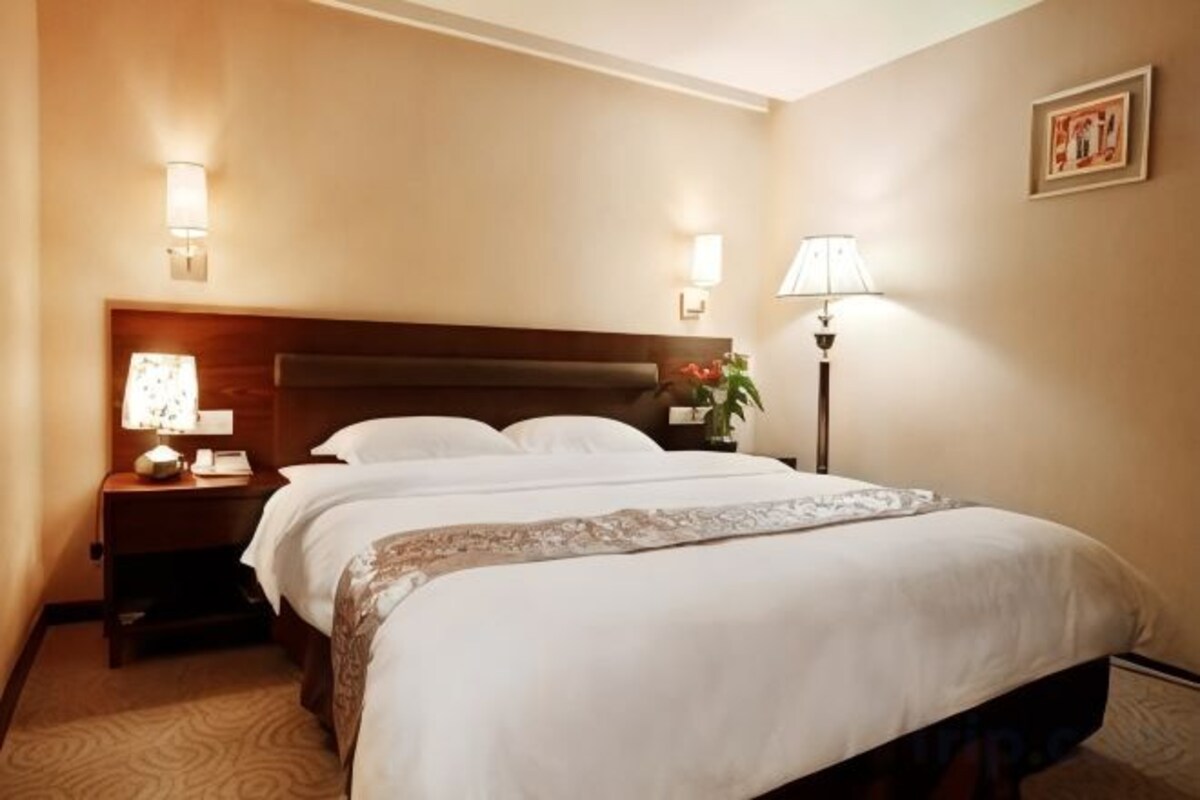 A hotel room with a large bed, two bedside tables, a nightstand, a lamp, and a framed picture on the wall.