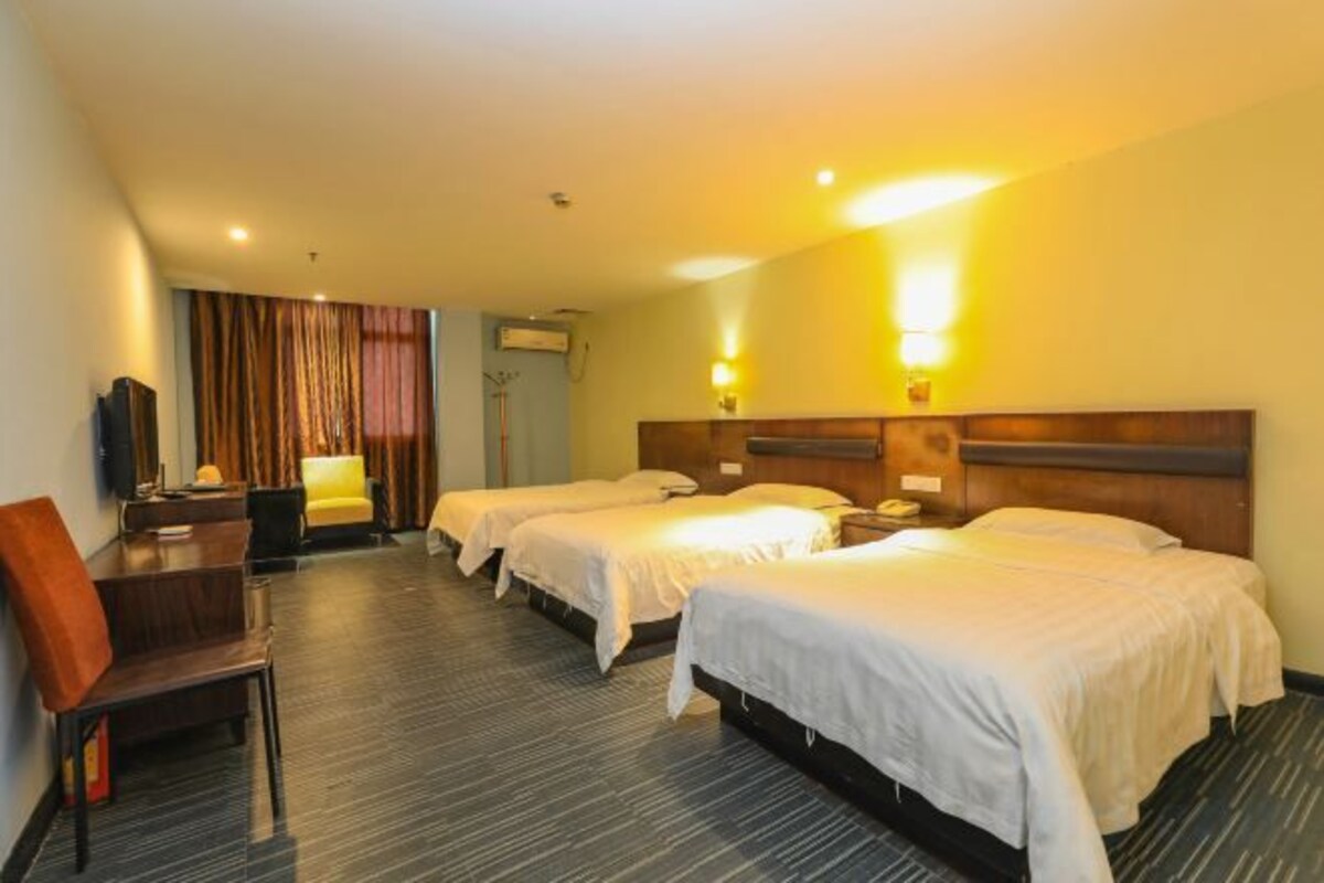 A hotel room with three beds, a desk, a chair, and a television.