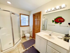 Une salle de bain avec une douche à l’italienne, des toilettes et un meuble-lavabo avec un miroir et des luminaires.