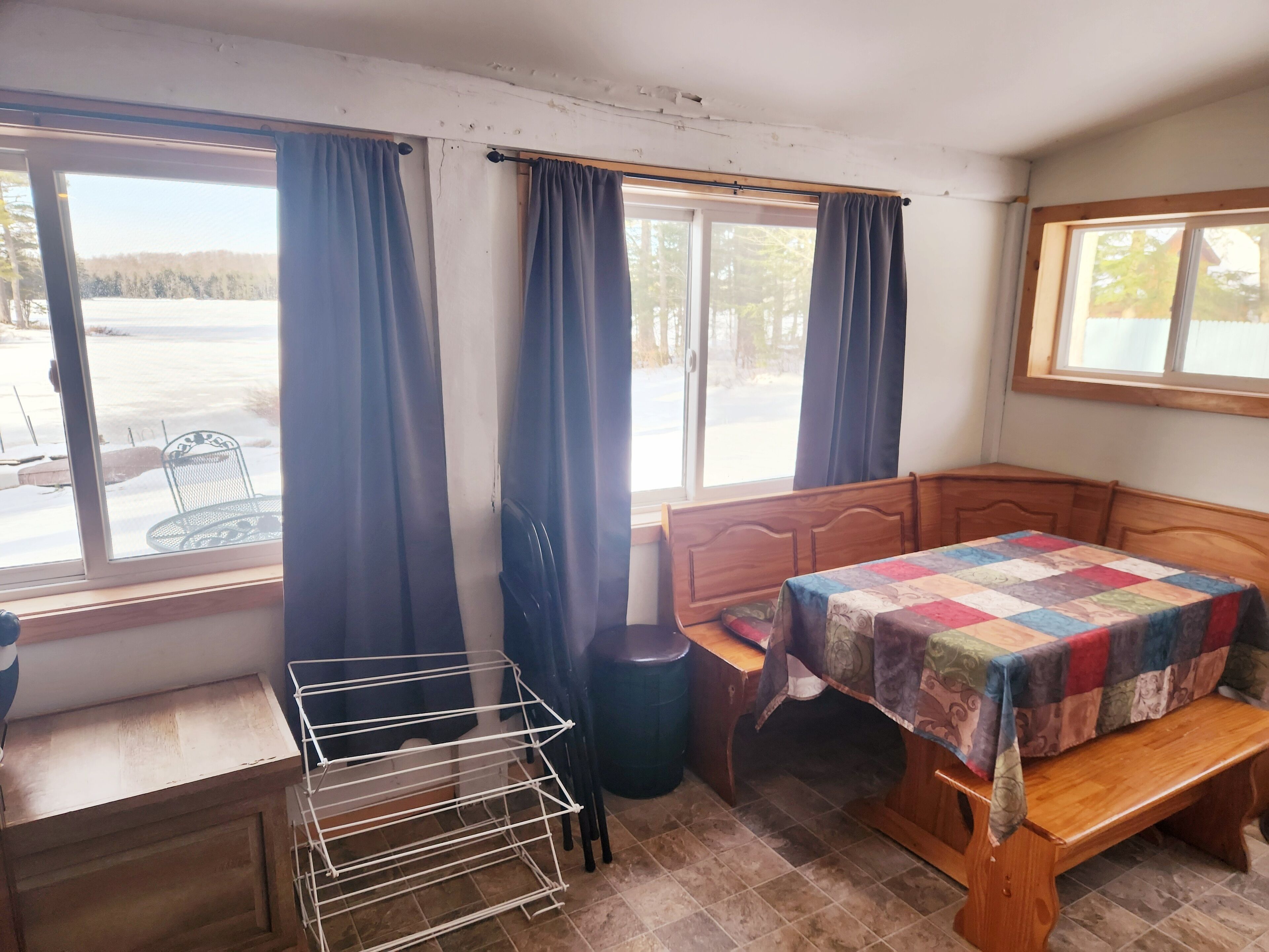 Una habitación con cama de madera, un banco, una mesita y un tendedero.