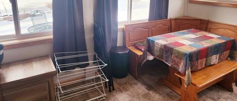 Una habitación con cama de madera, un banco, una mesita y un tendedero.